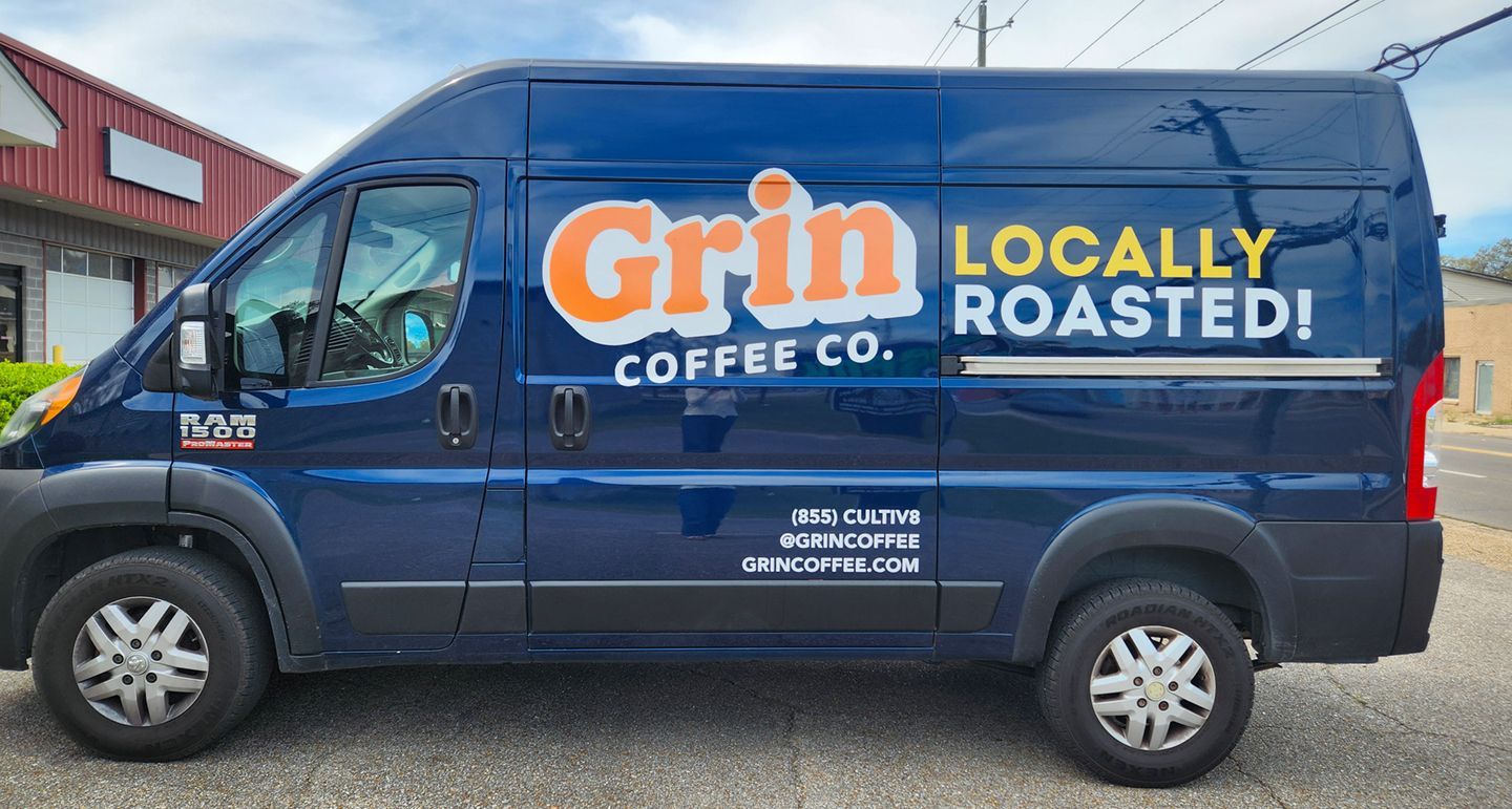 A blue Grin Coffee Co. cargo van parked outside, displaying the brand name and website on its side.