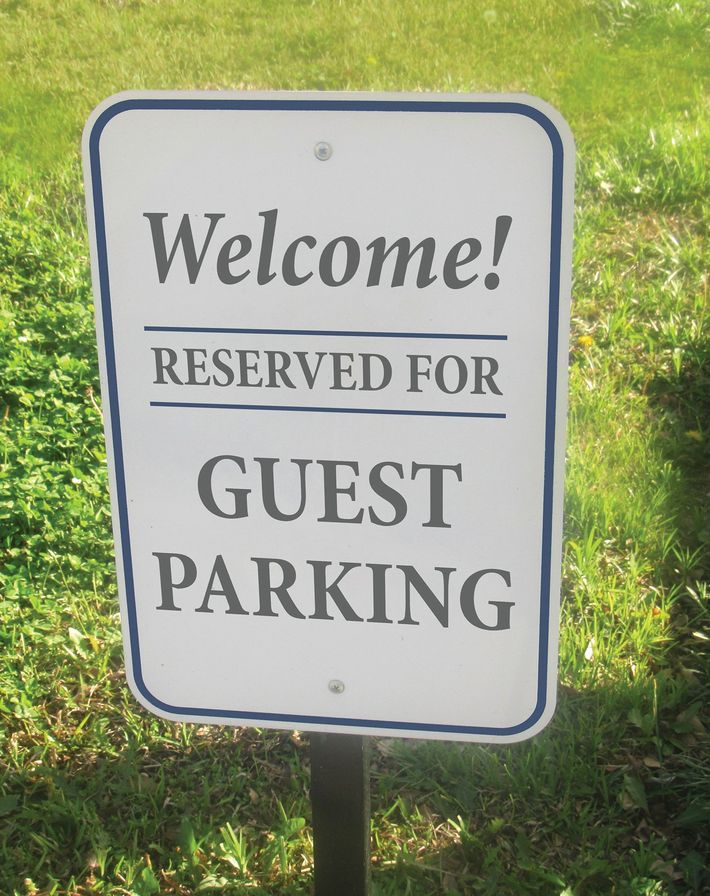 A white, rectangular parking sign with a blue border reads "Welcome! RESERVED FOR GUEST PARKING" in dark text.