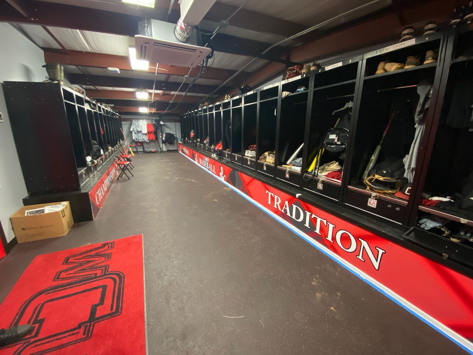 A locker room with black lockers, a red carpet with a logo, and red walls labeled 