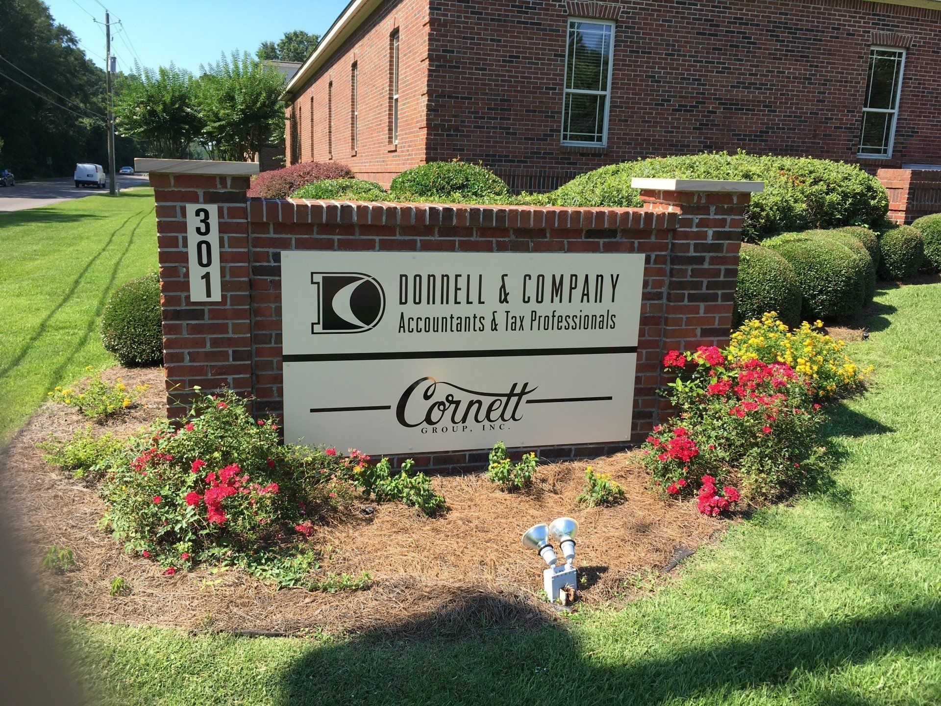 A brick sign for Judell & Company Accountants and Cornett Law Firm at 301, surrounded by a garden on a sunny day.