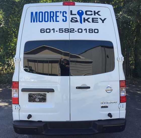 Rear view of a white Moore's Lock & Key van with the phone number 601-582-0180 printed on the back doors.