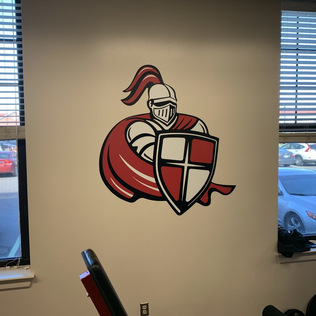 A red and white knight mural on a wall, depicted from the waist up, holding a shield with a cross design.