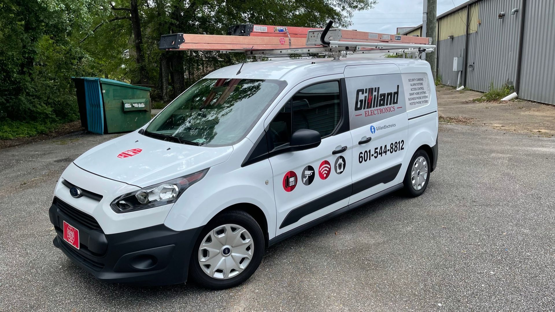 A white Gilland Heating and Cooling work van parked on a gravel lot with a ladder rack on top.