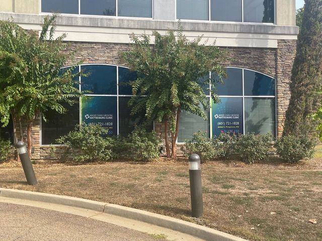 Two ground-floor office windows with blue advertisements and branding, framed by stone siding, trees, and landscaping.