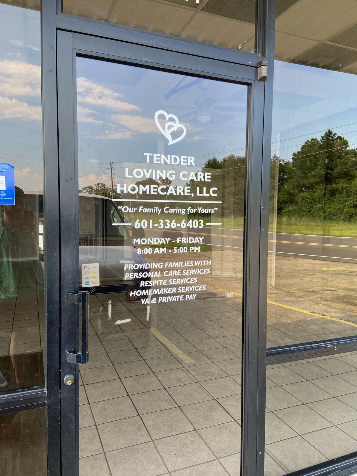 Glass front door of Tender Loving Care Homecare, LLC, displaying business hours, contact info, and services.