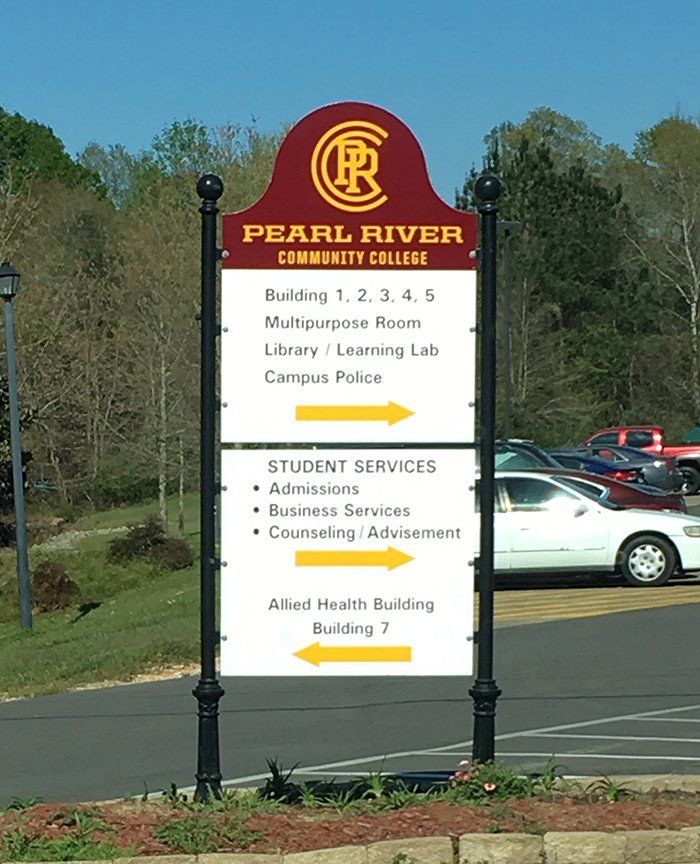 A maroon and white Pearl River Community College directional sign with yellow arrows listing buildings and offices.