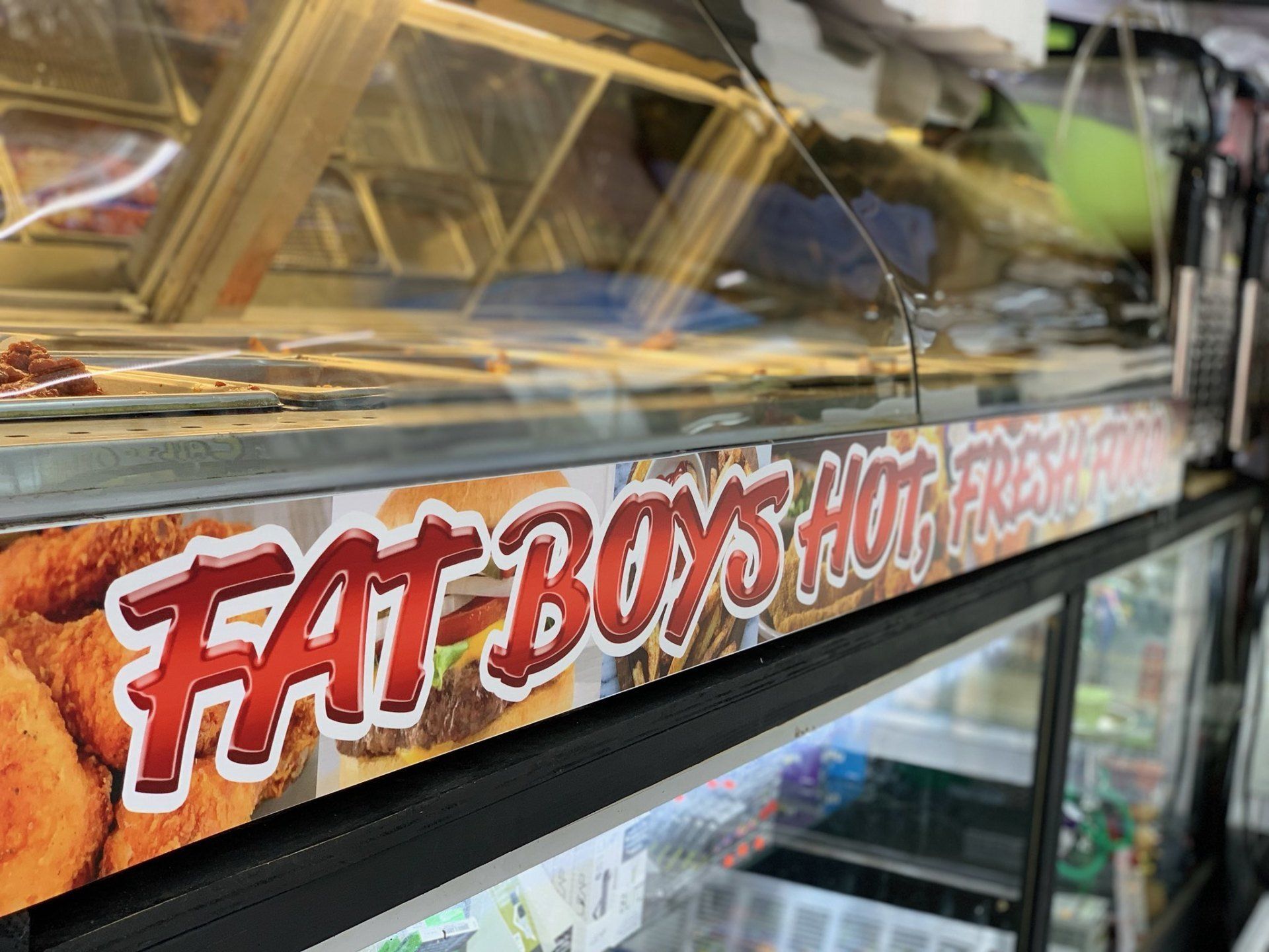 A food warmer display case at a deli or takeaway counter featuring a sign that reads 