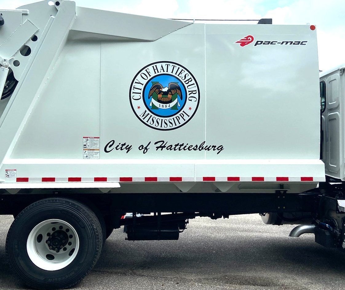 A side view of a white City of Hattiesburg sanitation truck featuring the city seal and logo.