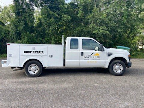 A white Matlock Roof Repair utility truck parked on a gravel lot with trees in the background.