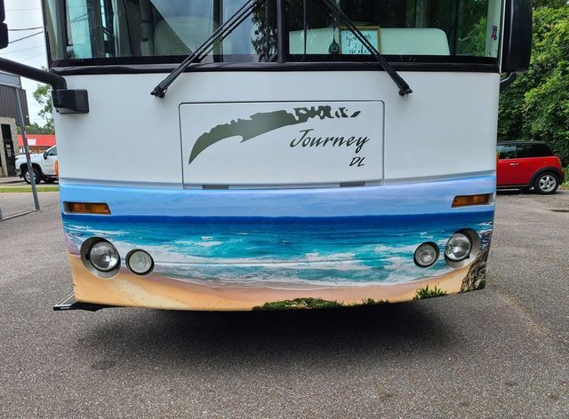 The front of a white RV featuring a custom mural of a blue ocean beach scene painted across the bumper.