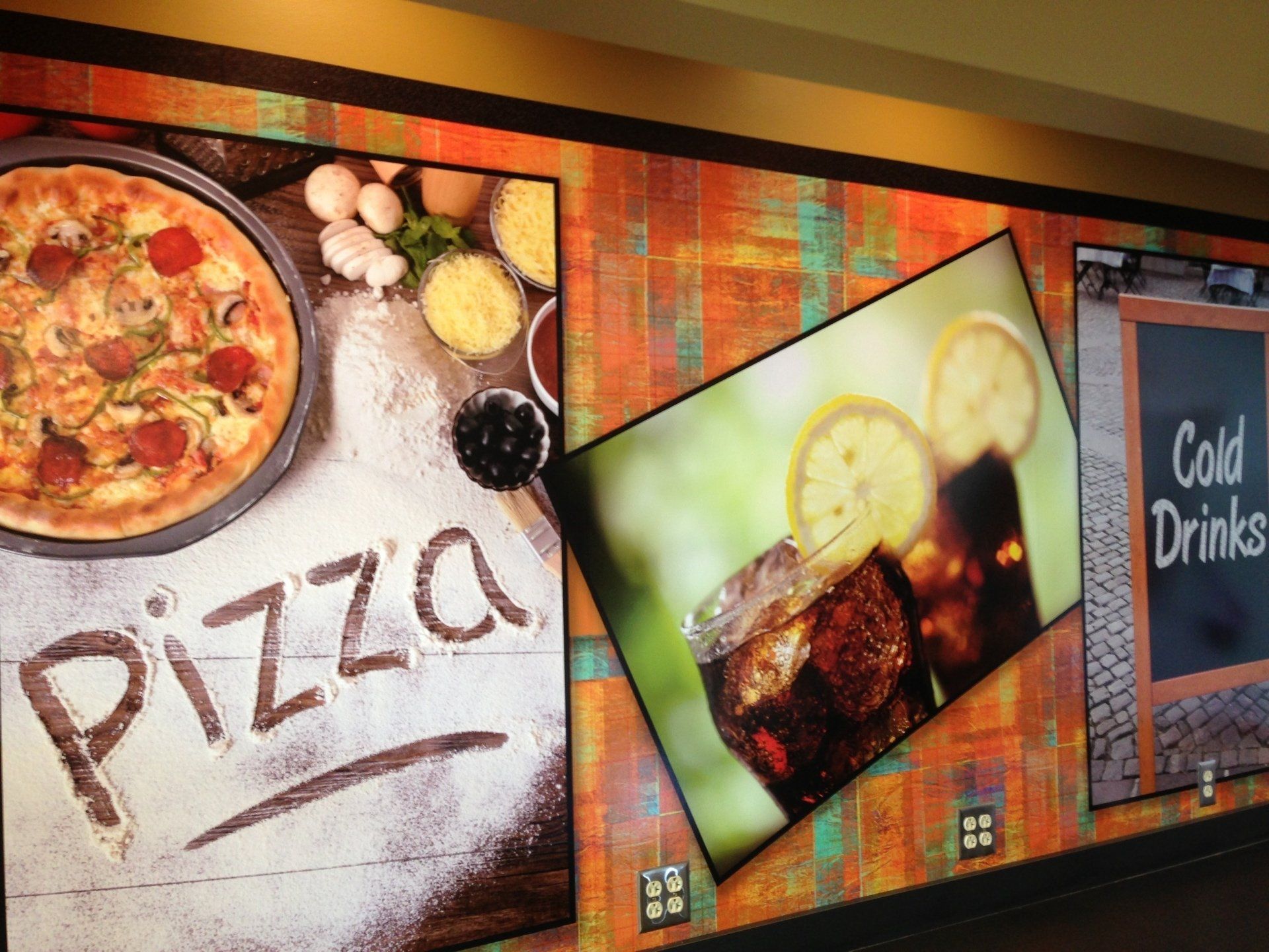 A wall display featuring a pizza with toppings, a glass of cola with lemon, and a sign that reads 