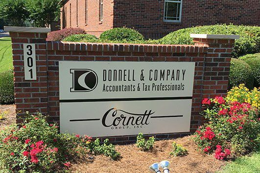 A brick sign for Donnell & Company and Cornett Asset Management in a landscaped garden with red flowers.