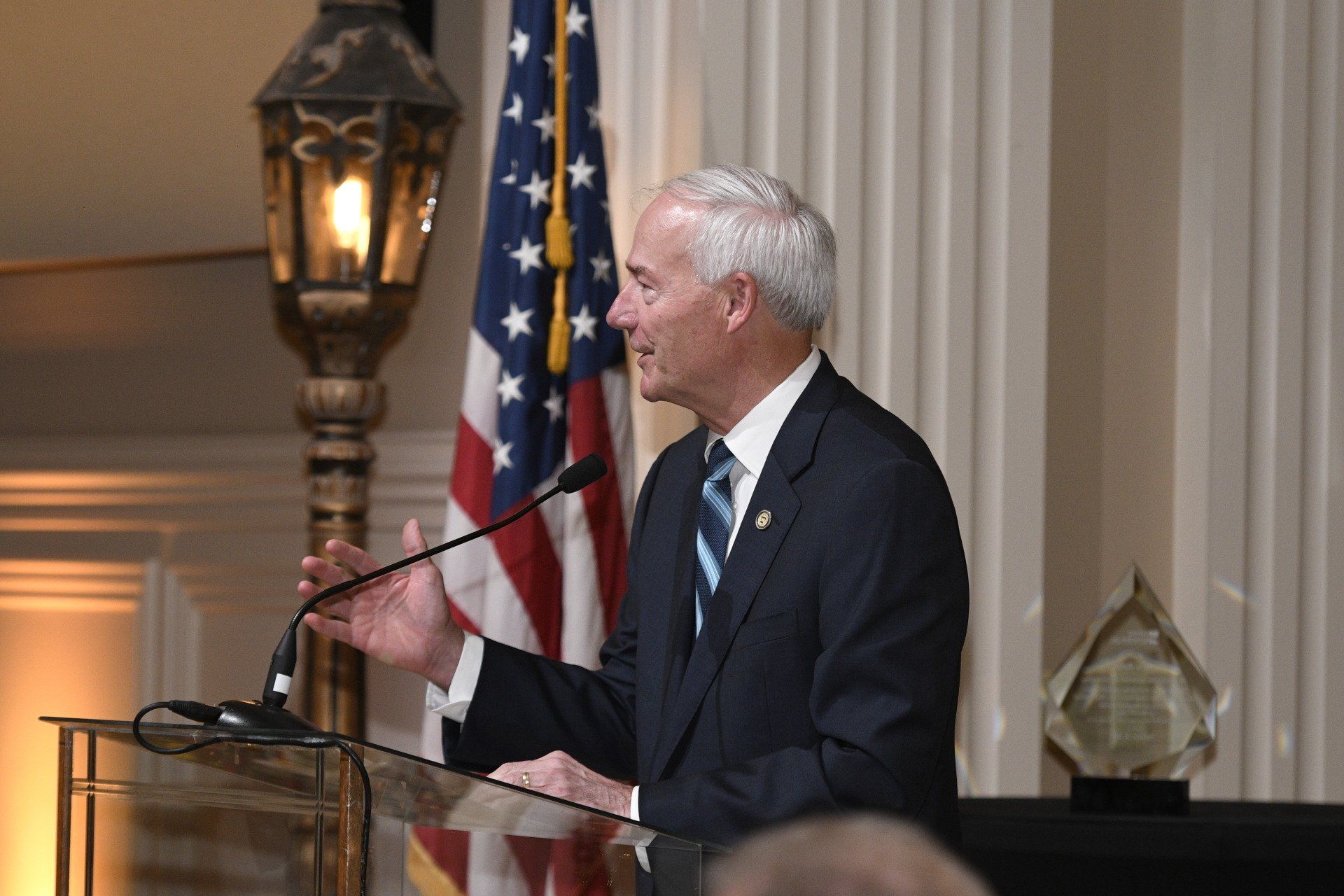 A man in a suit and tie is standing at a podium speaking into a microphone.