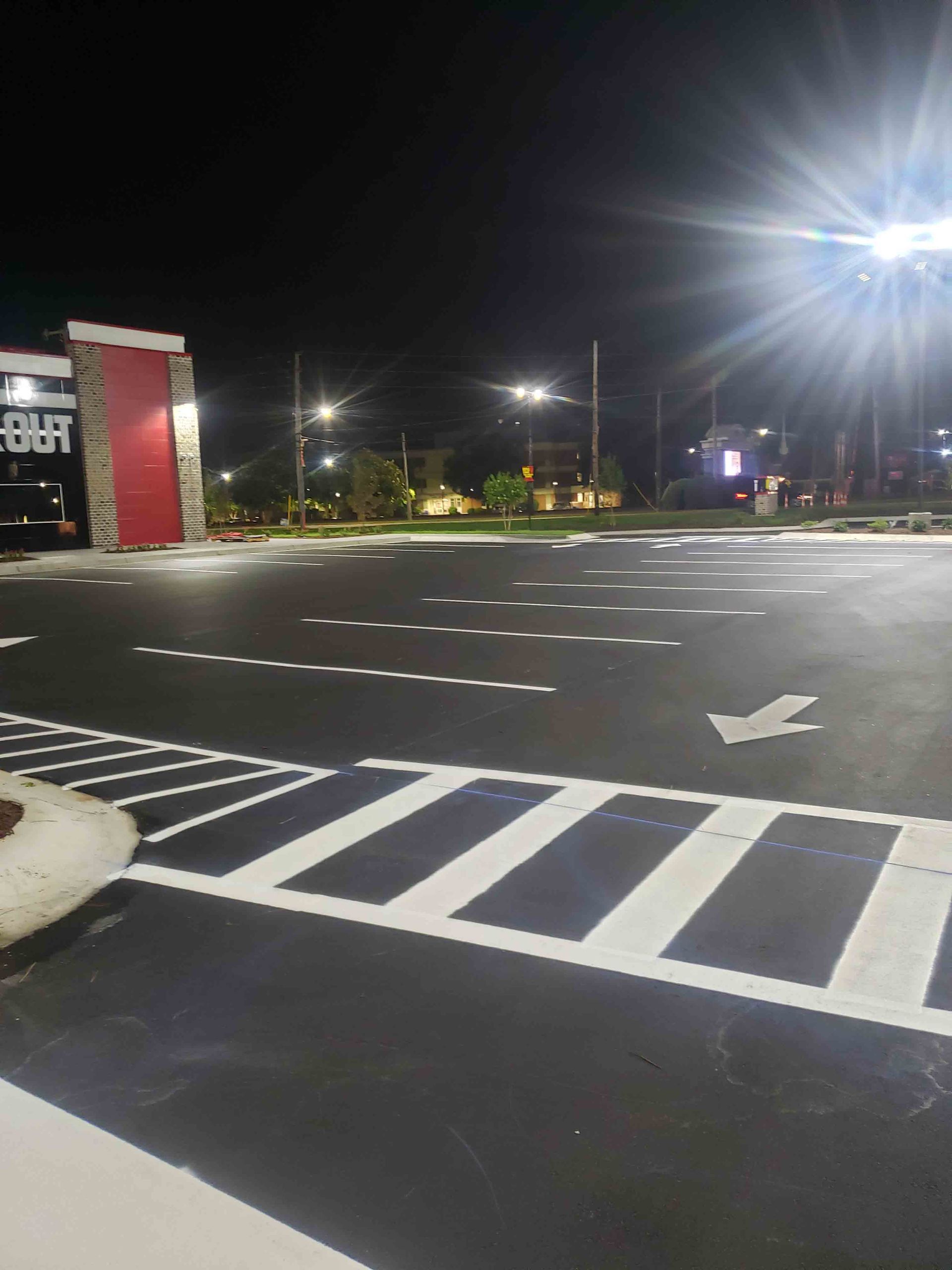A parking lot at night with a red building in the background