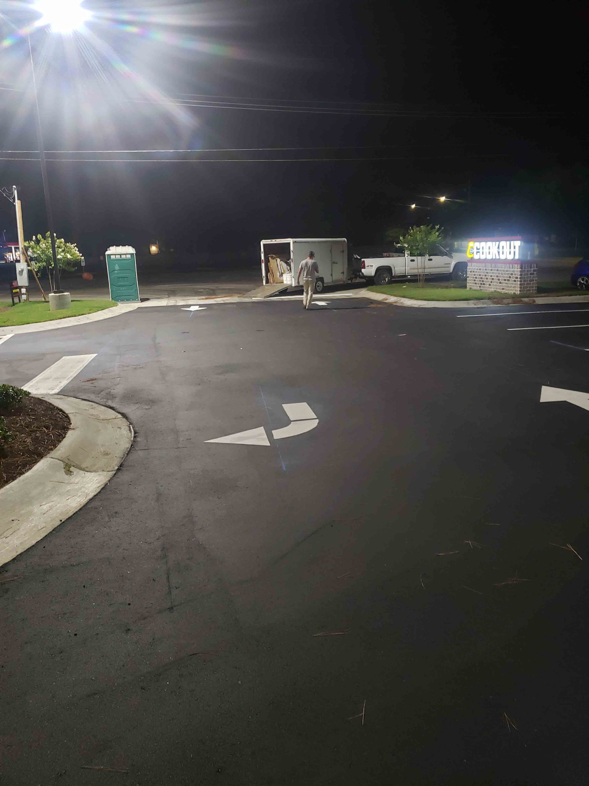 A parking lot is lit up at night with a white arrow pointing to the right.