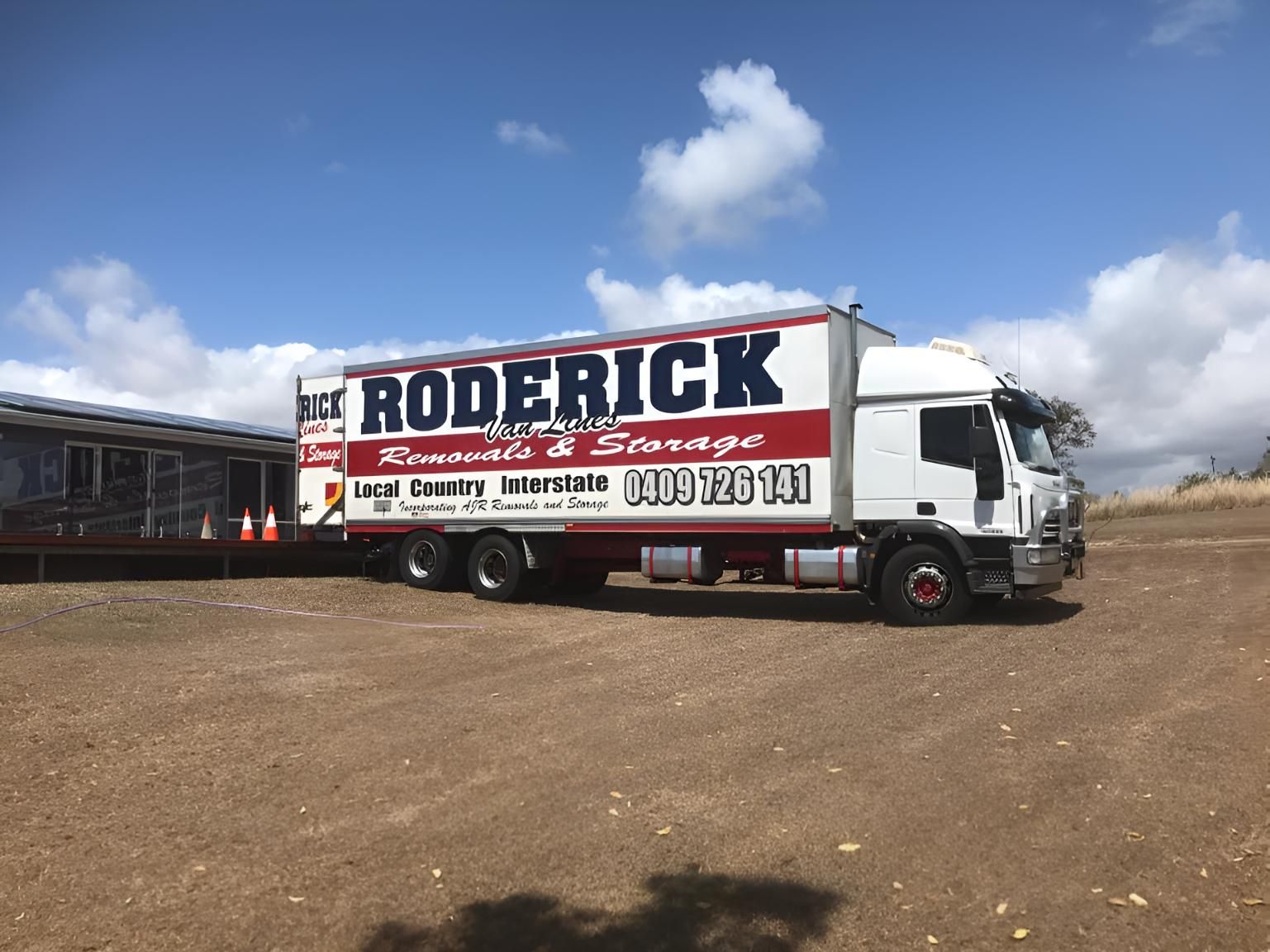 A Red and White Roderick Truck is Parked in a Dirt Field — Roderick Removals & Van Lines In Toowoomba, QLD