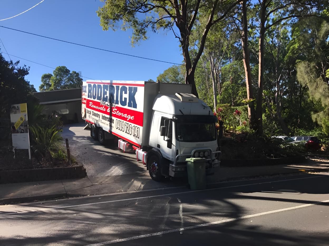 A Red and White Moving Truck is Parked on the Side of the Road — Roderick Removals & Van Lines In Gladstone Central, QLD