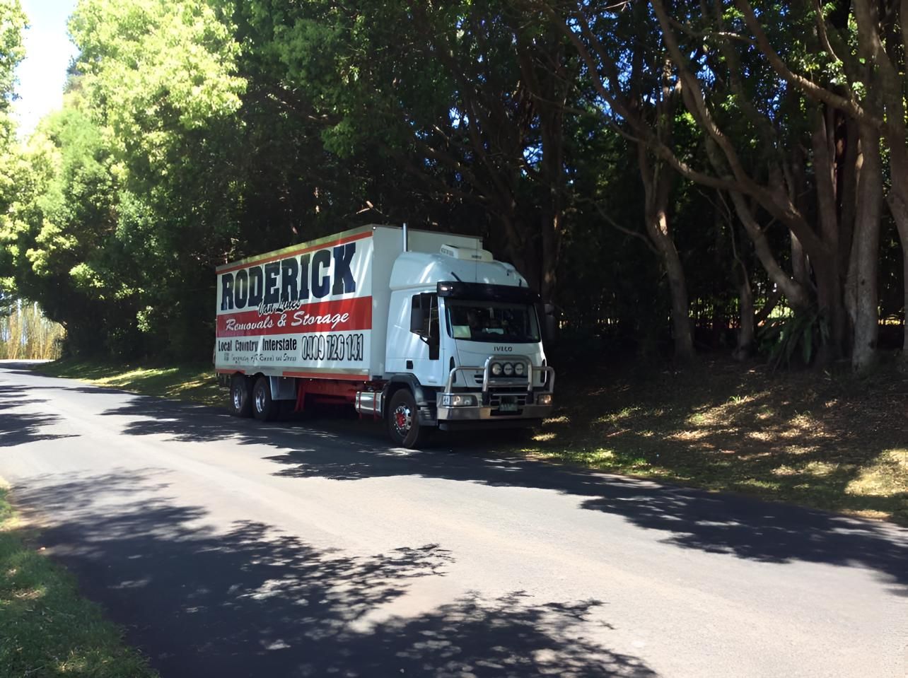 A Frederick Truck is Driving Down a Road Surrounded by Trees — Roderick Removals & Van Lines In Gladstone Central, QLD