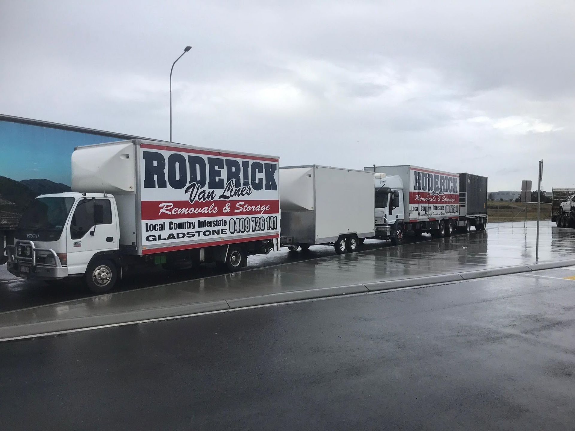 Line of Removalists Gladstone trucks parked on a wet roadside.