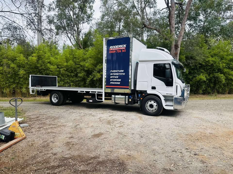 A White Truck With a Blue Box on the Back is Parked in a Gravel Lot — Roderick Removals & Van Lines In Agnes Water, NSW