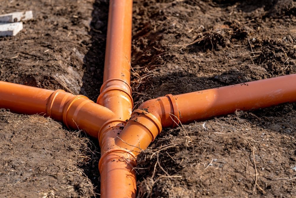 Orange plastic pipes joined underground in a Y-shaped trench on bare soil