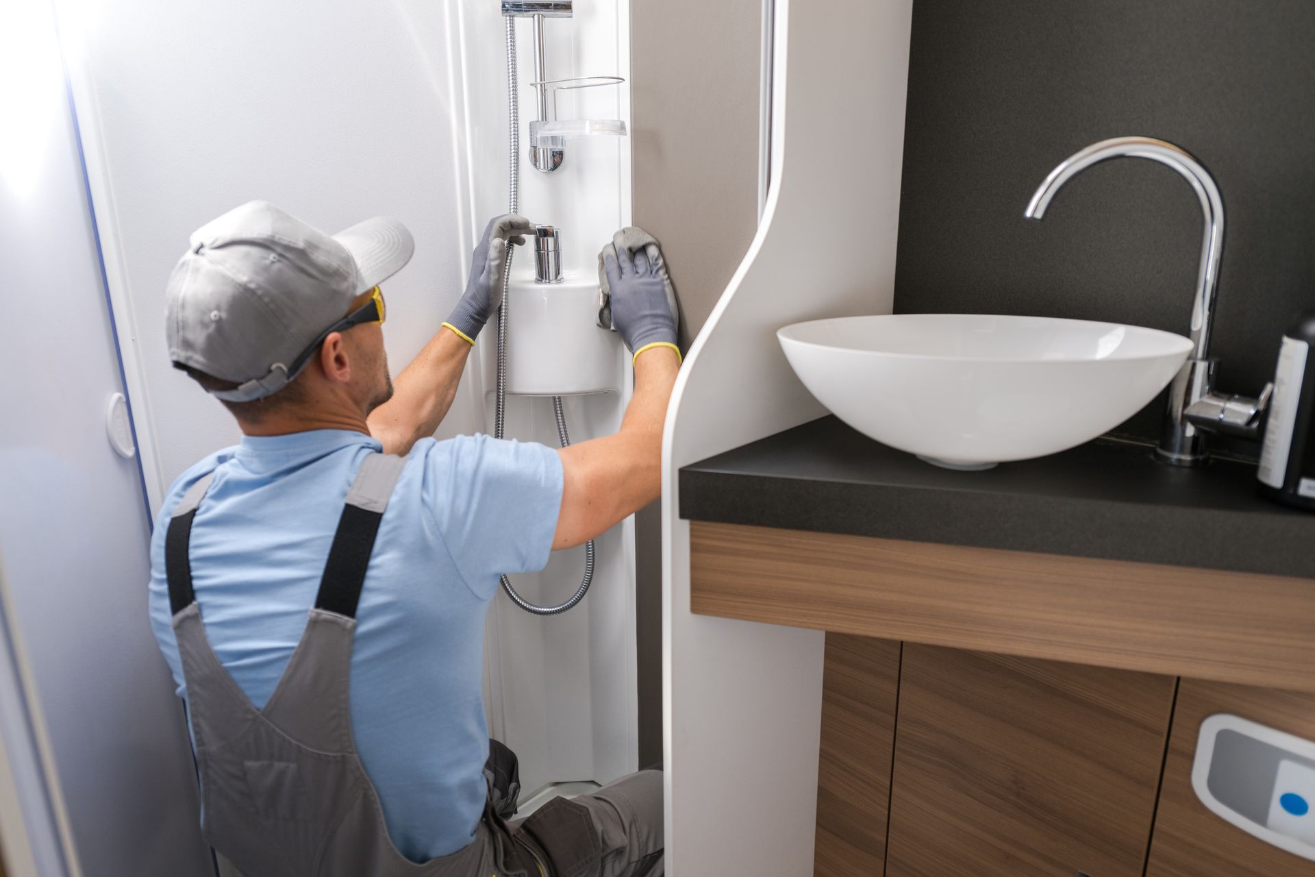 Plumber repairing a shower pipe beside a bathroom sink and vanity.