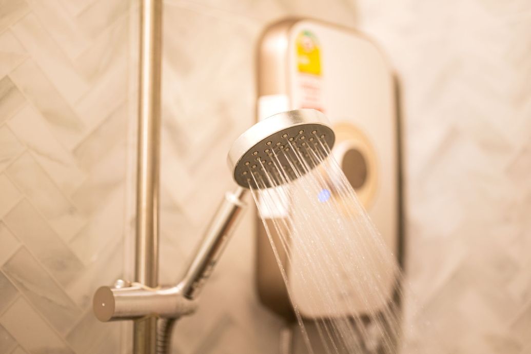 Showerhead spraying water in a tiled bathroom, with a water heater in the background
