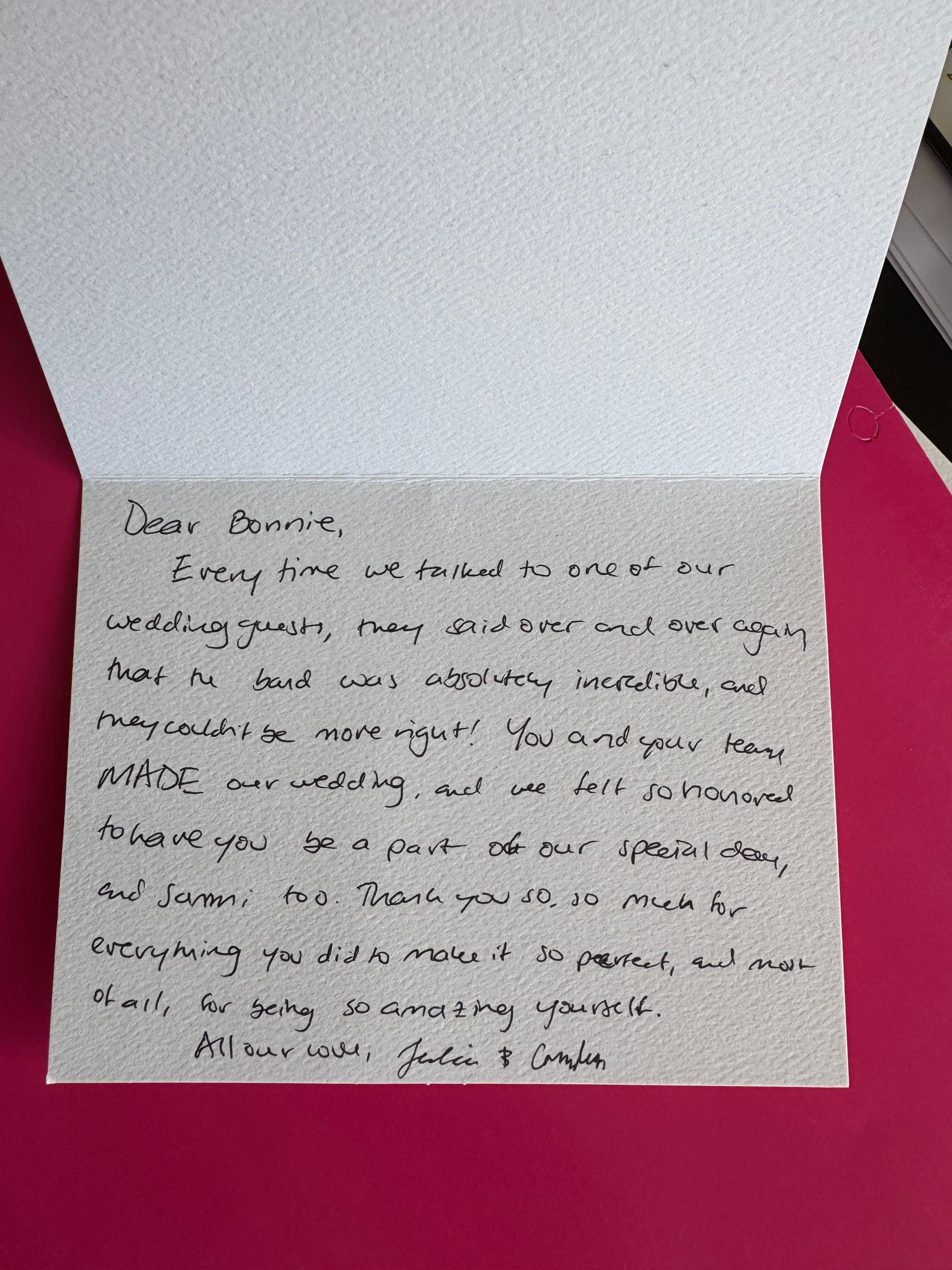 A handwritten note inside a white card on a pink surface. The message is addressed to