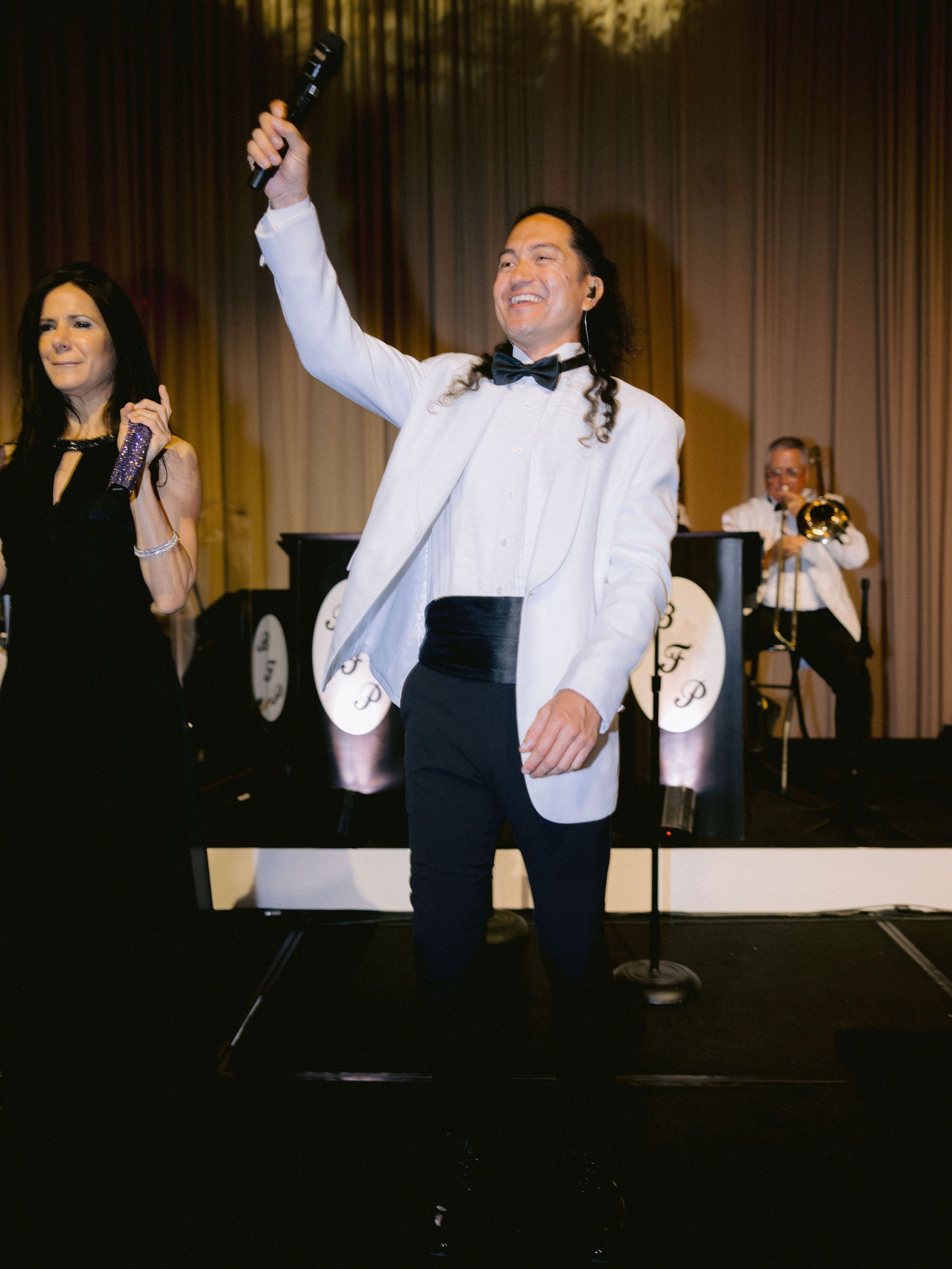 A man in a tuxedo is holding a microphone in front of a woman in a black dress