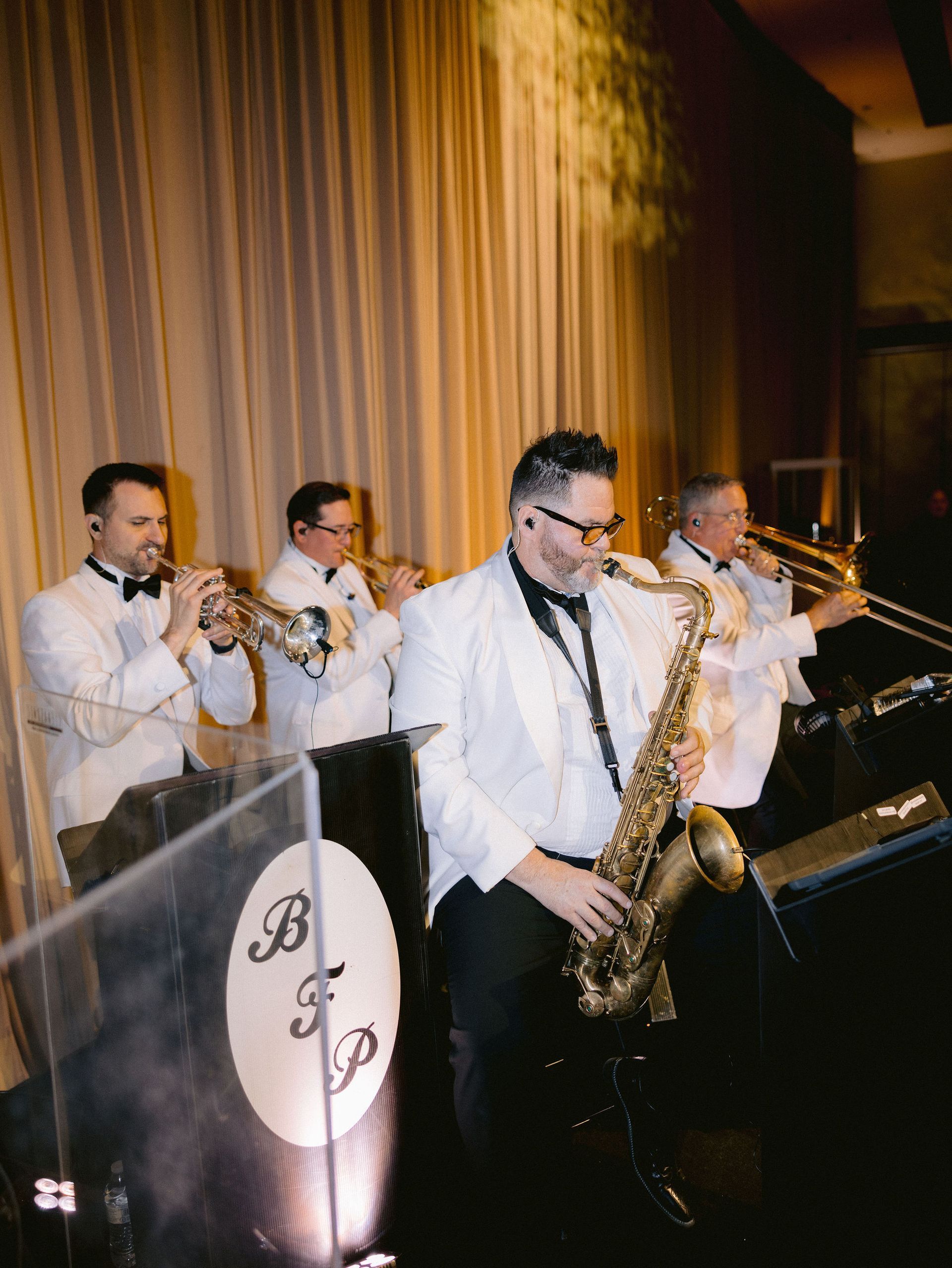 A group of men in tuxedos are playing saxophones and trumpets on a stage.