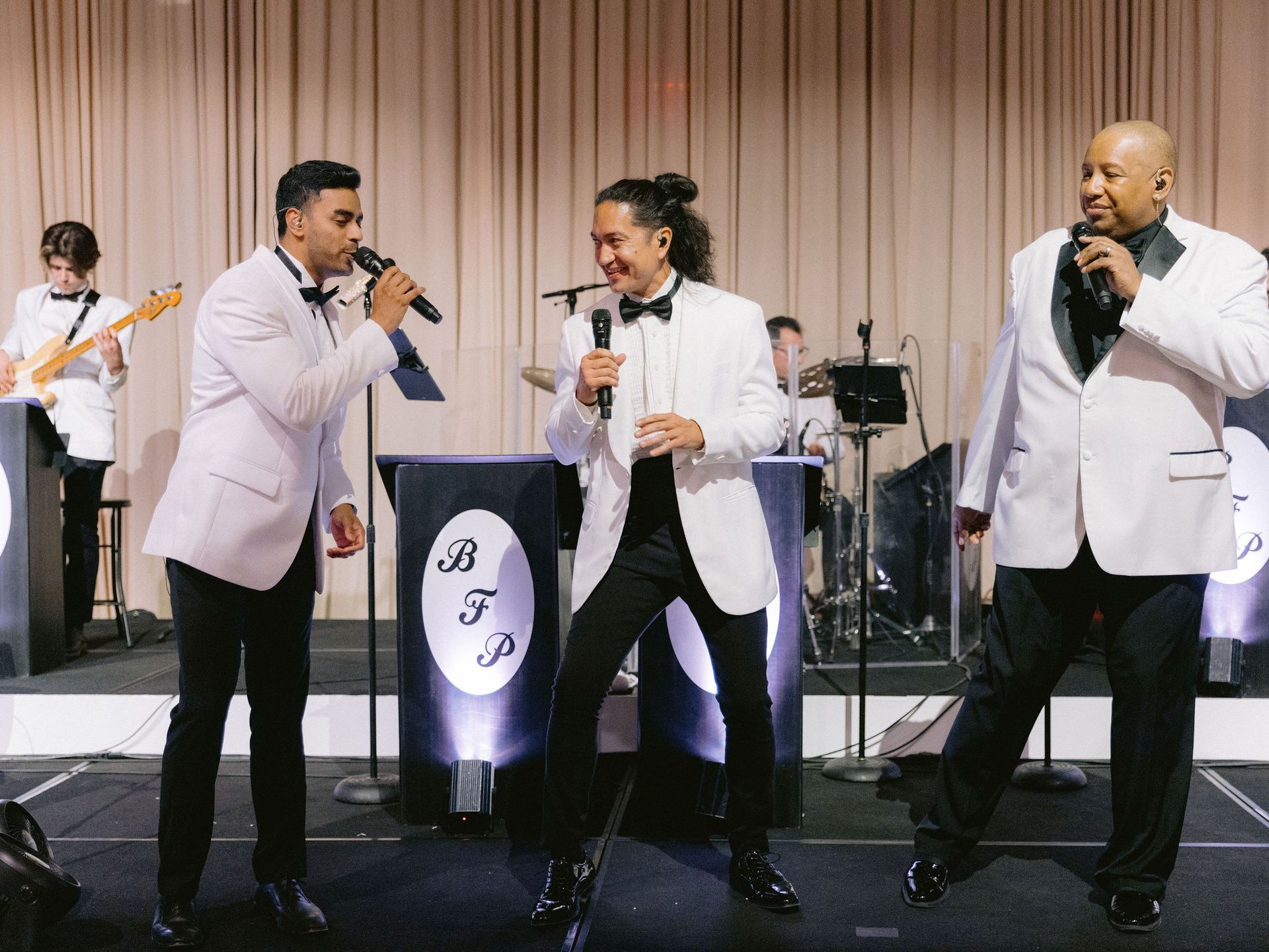 A group of men in tuxedos are singing into microphones on a stage.