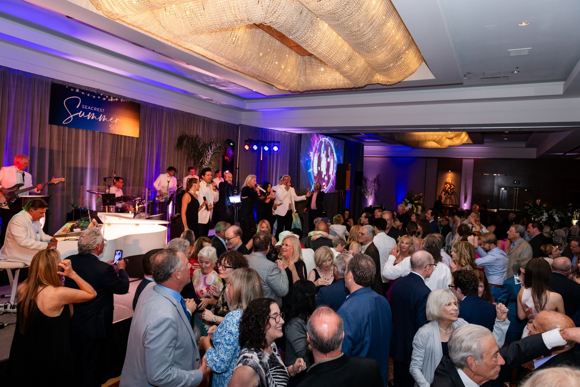 People dancing at a formal event with a band performing on stage; elegant ballroom.