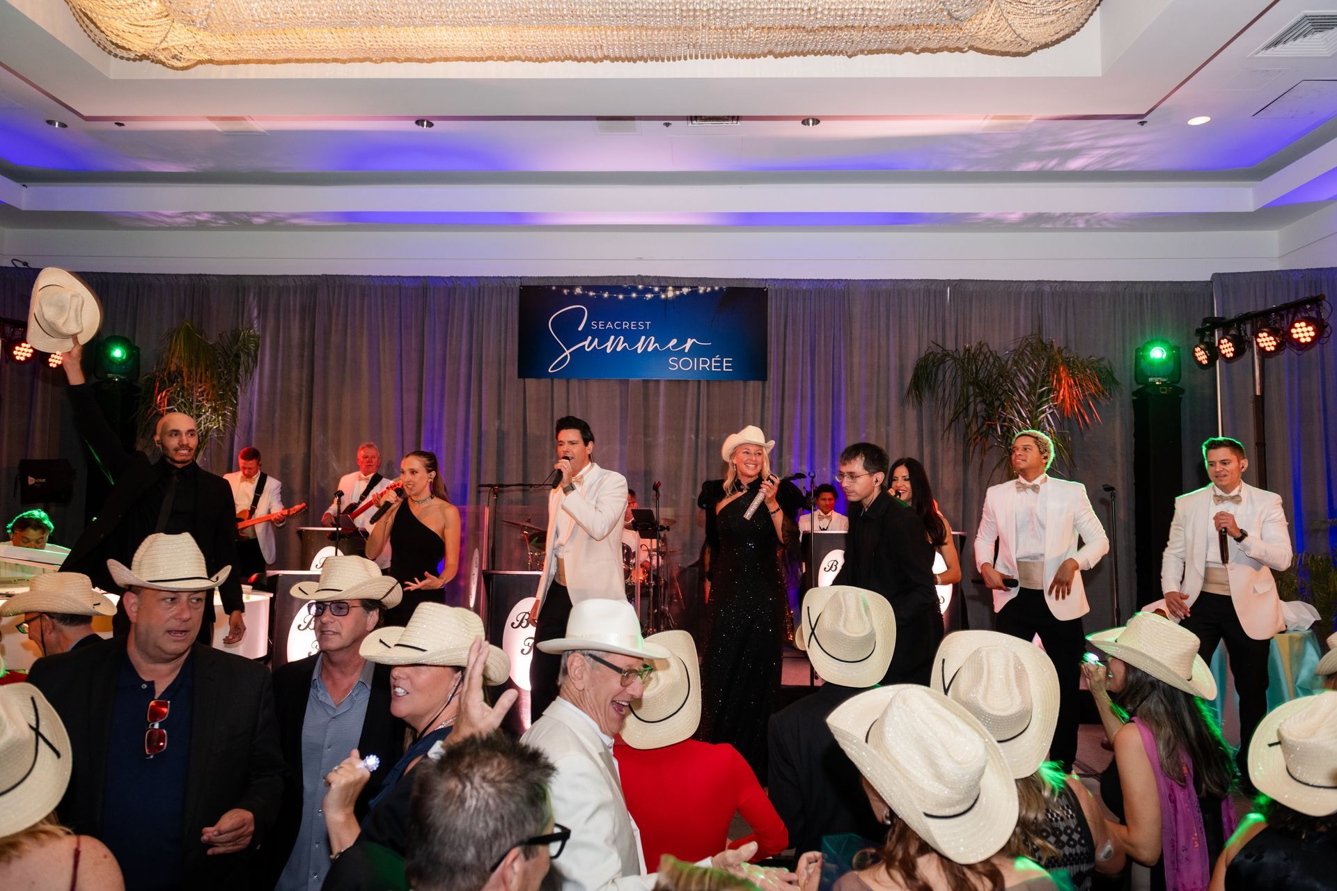 Band performing on stage at a party; people in cowboy hats dancing and socializing.