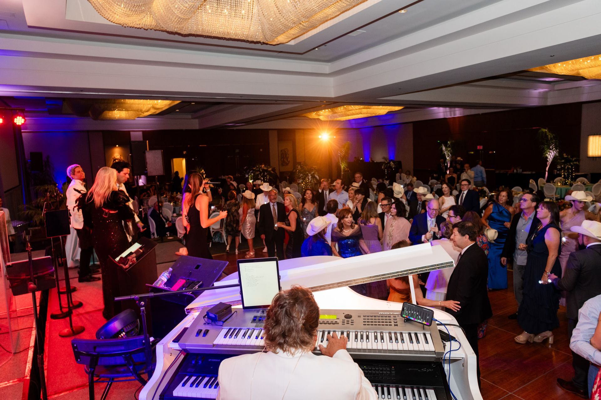 A band performs at a formal event, with guests dancing in a large ballroom.