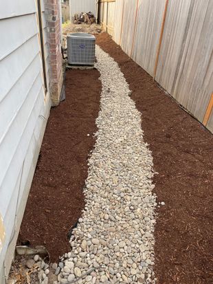 Narrow side yard with a white gravel path between house siding and a wooden fence.