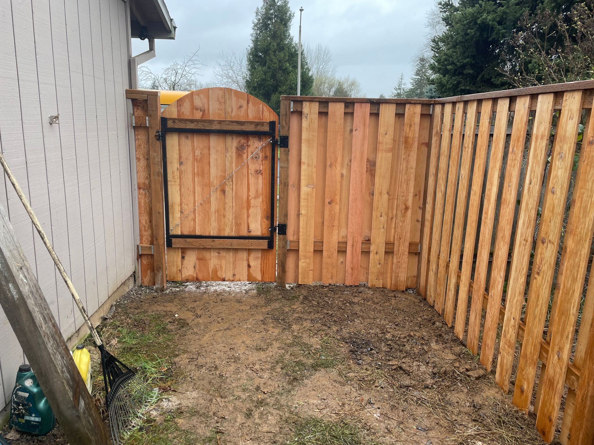 Small fenced backyard corner with a wooden gate, white wall, and bare dirt ground.