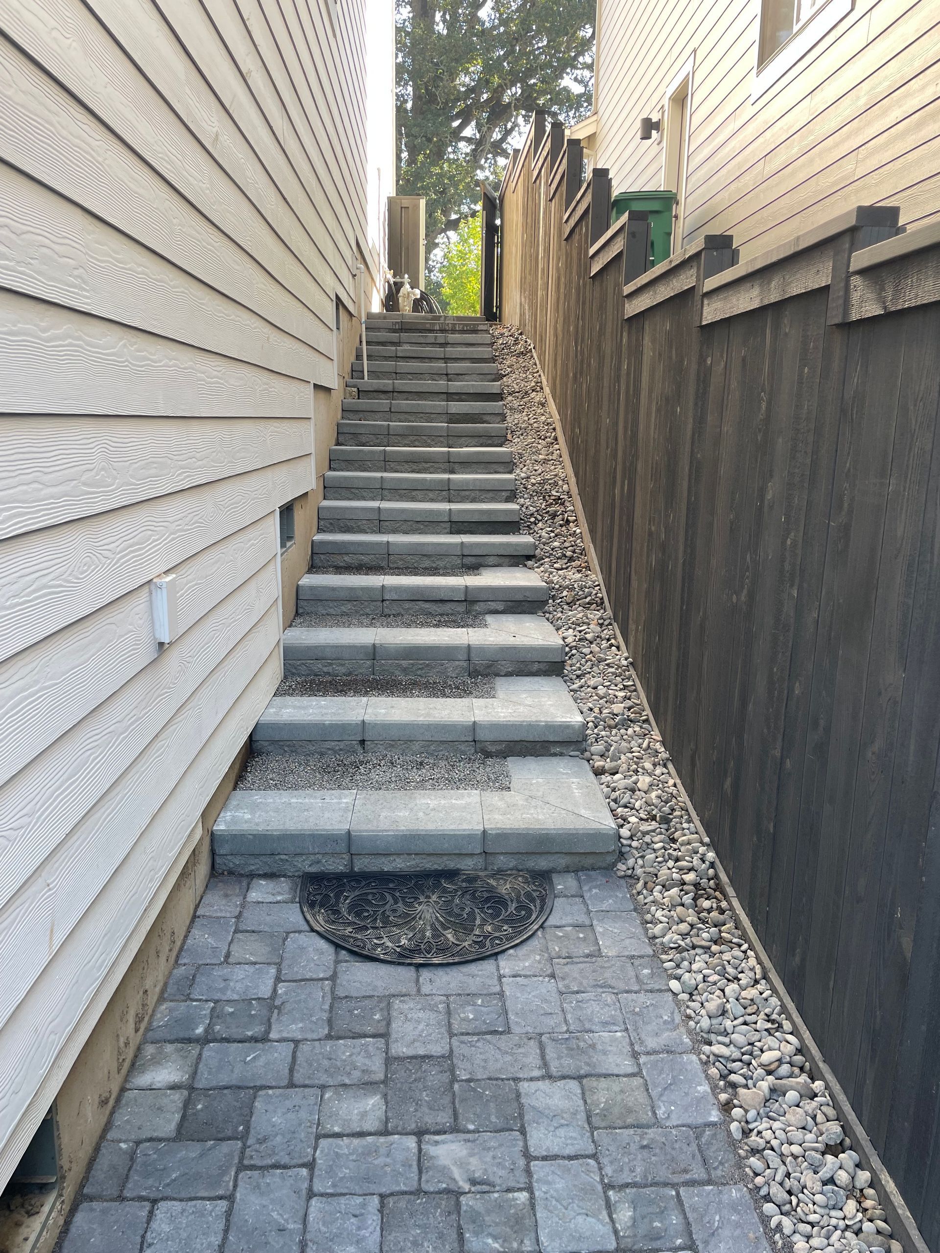 Narrow outdoor stairway between houses, with stone pavers and a gravel-lined retaining wall.