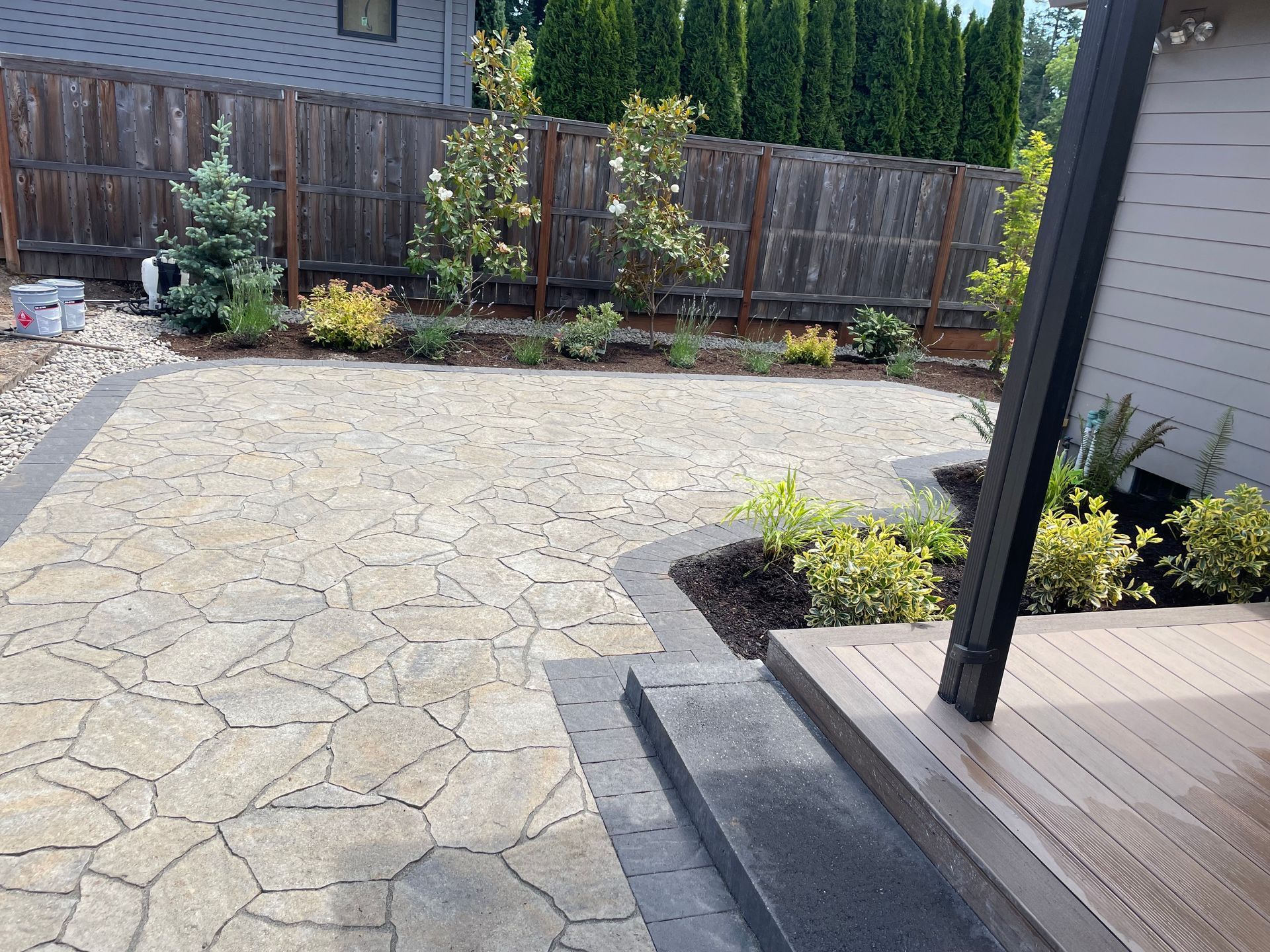 Backyard patio with stamped concrete, wooden deck steps, and landscaped fence line