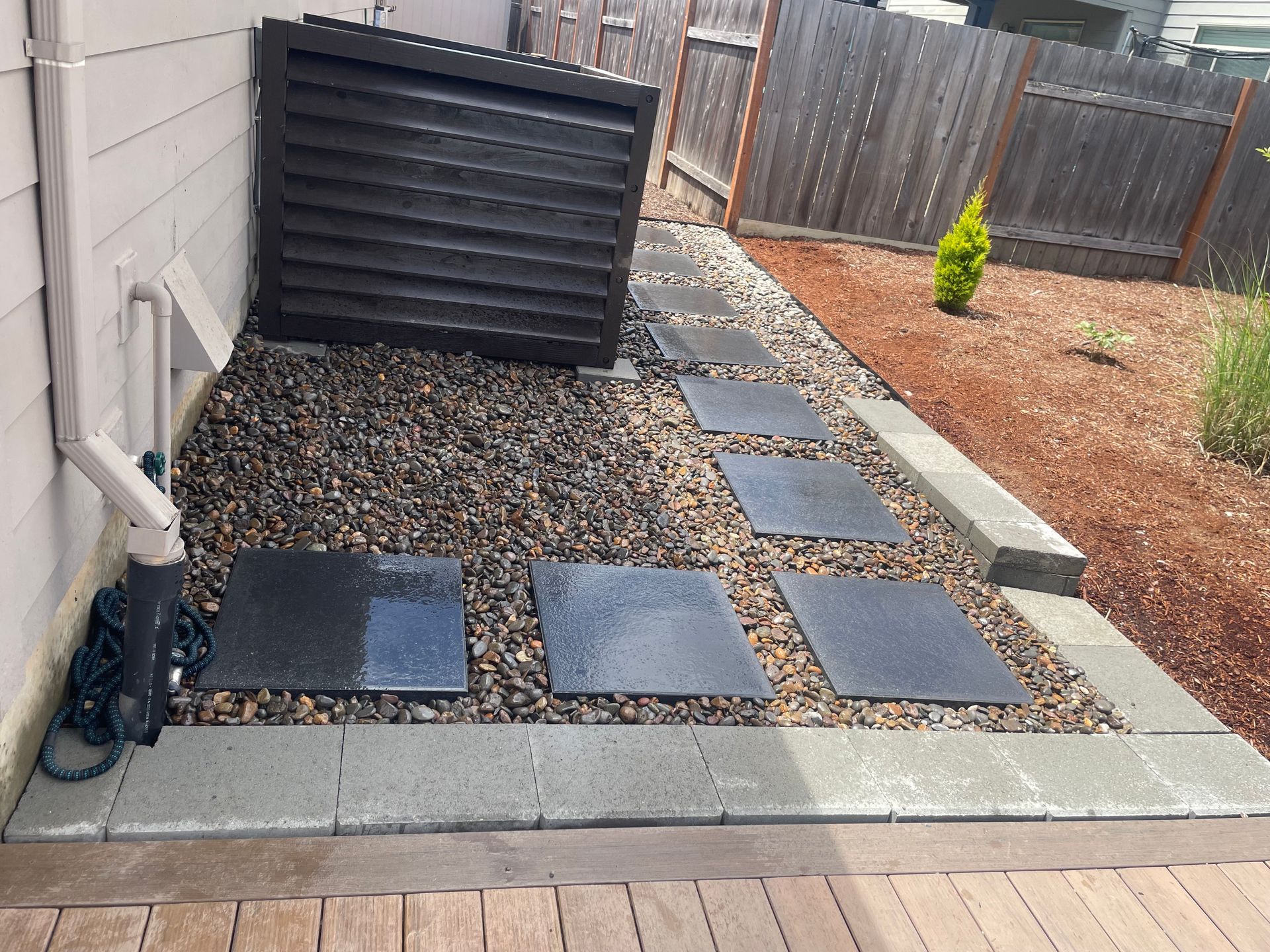 Small gravel side yard with stepping stones, concrete border, and an outdoor HVAC unit beside a house.