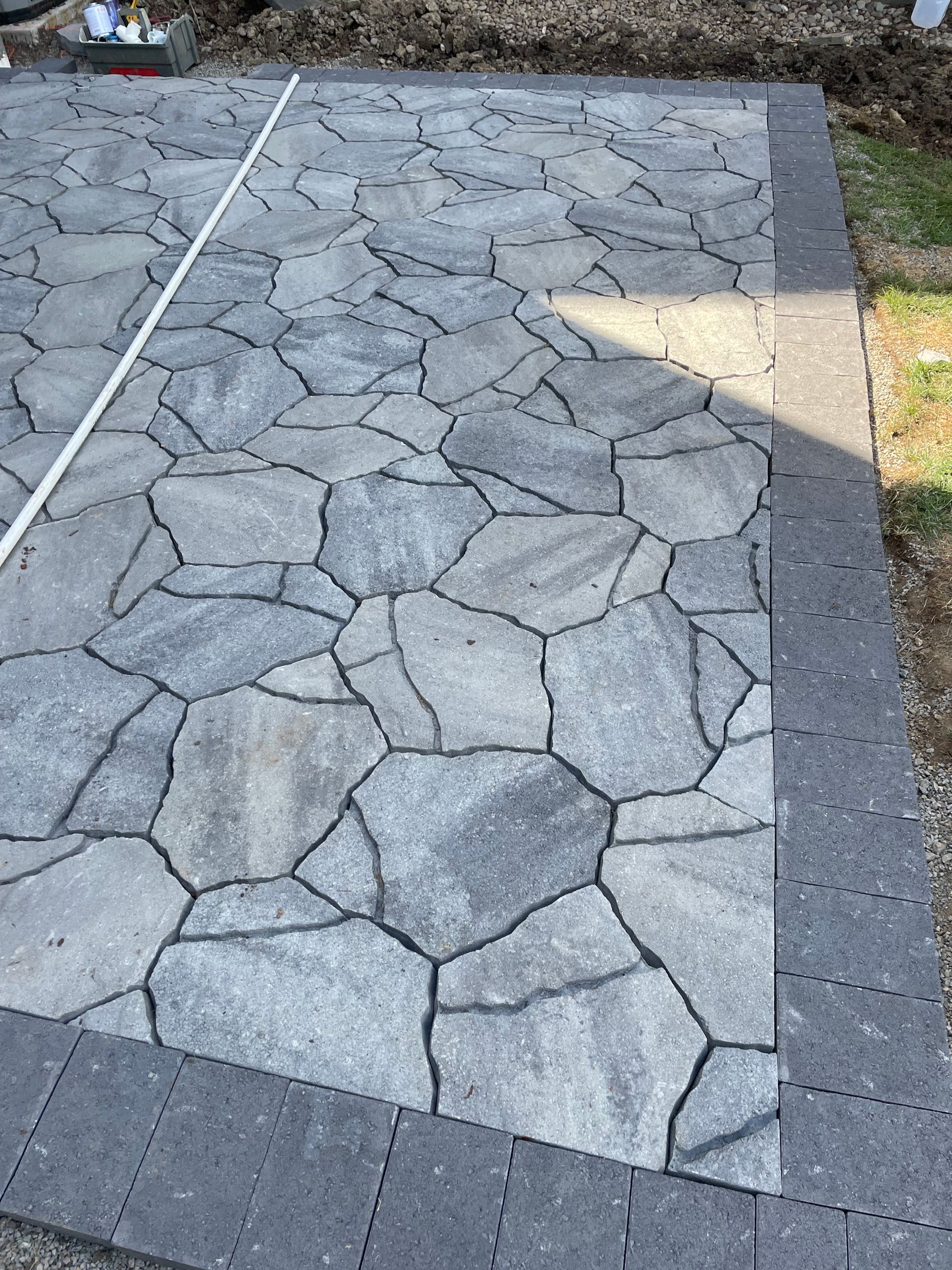 Stone-pattern concrete walkway bordered by dark pavers and gravel, with sunlight on one side