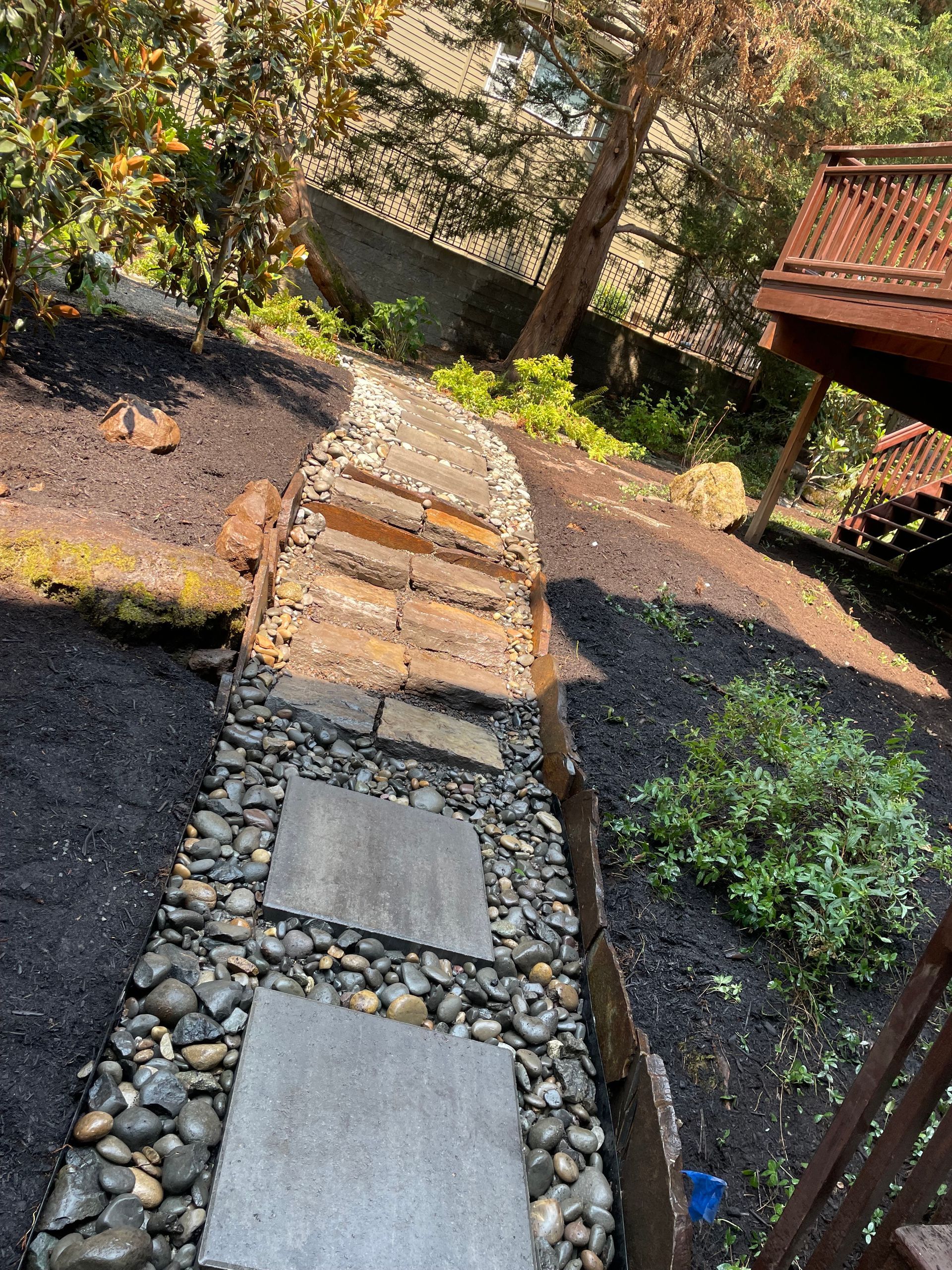 Steep garden path with stone steps and gravel, bordered by plants and a wooden fence