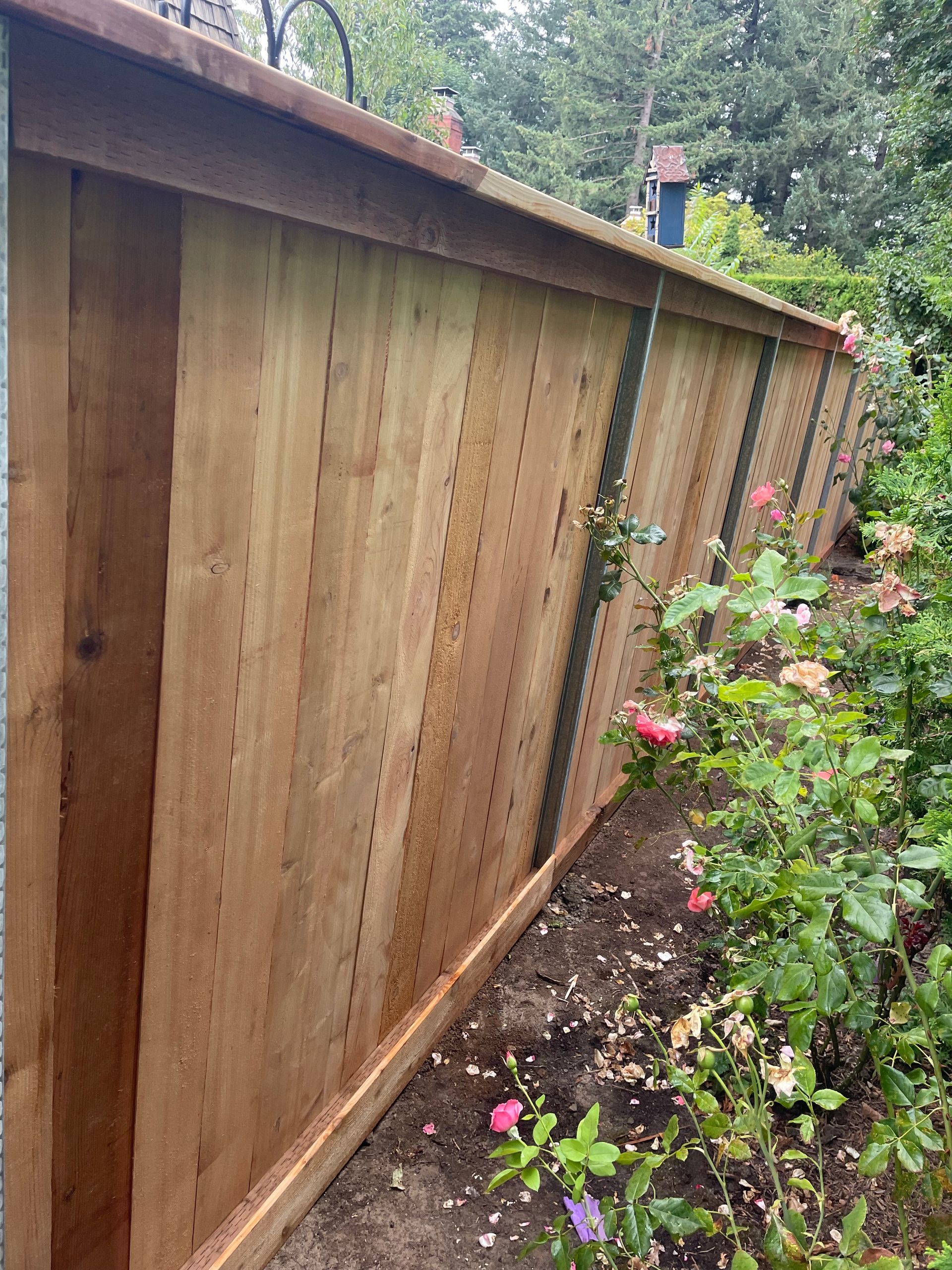 Wooden fence beside a flower garden, viewed from an angle in a backyard.