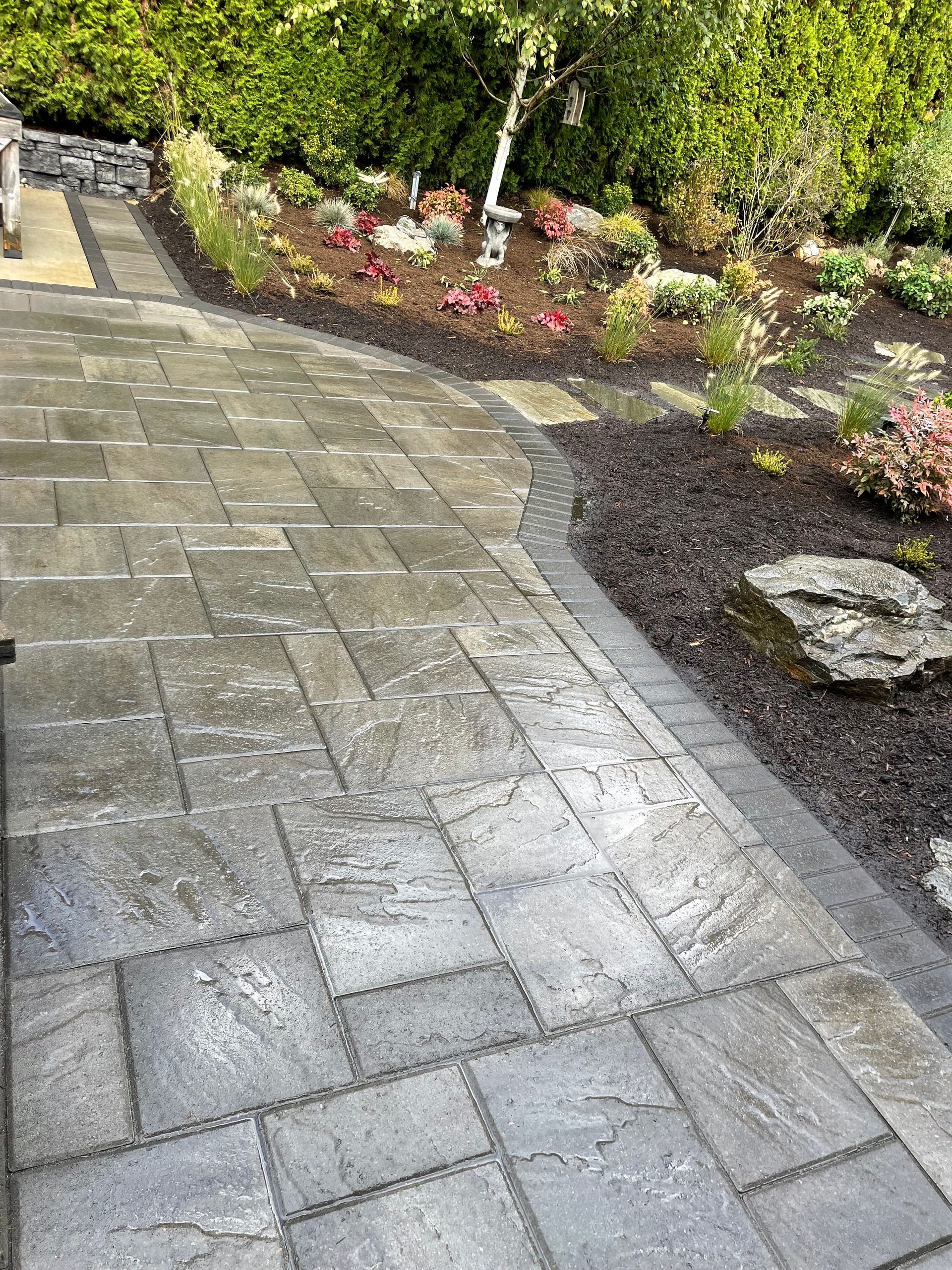 Wet stone patio beside a garden bed with flowers and shrubs