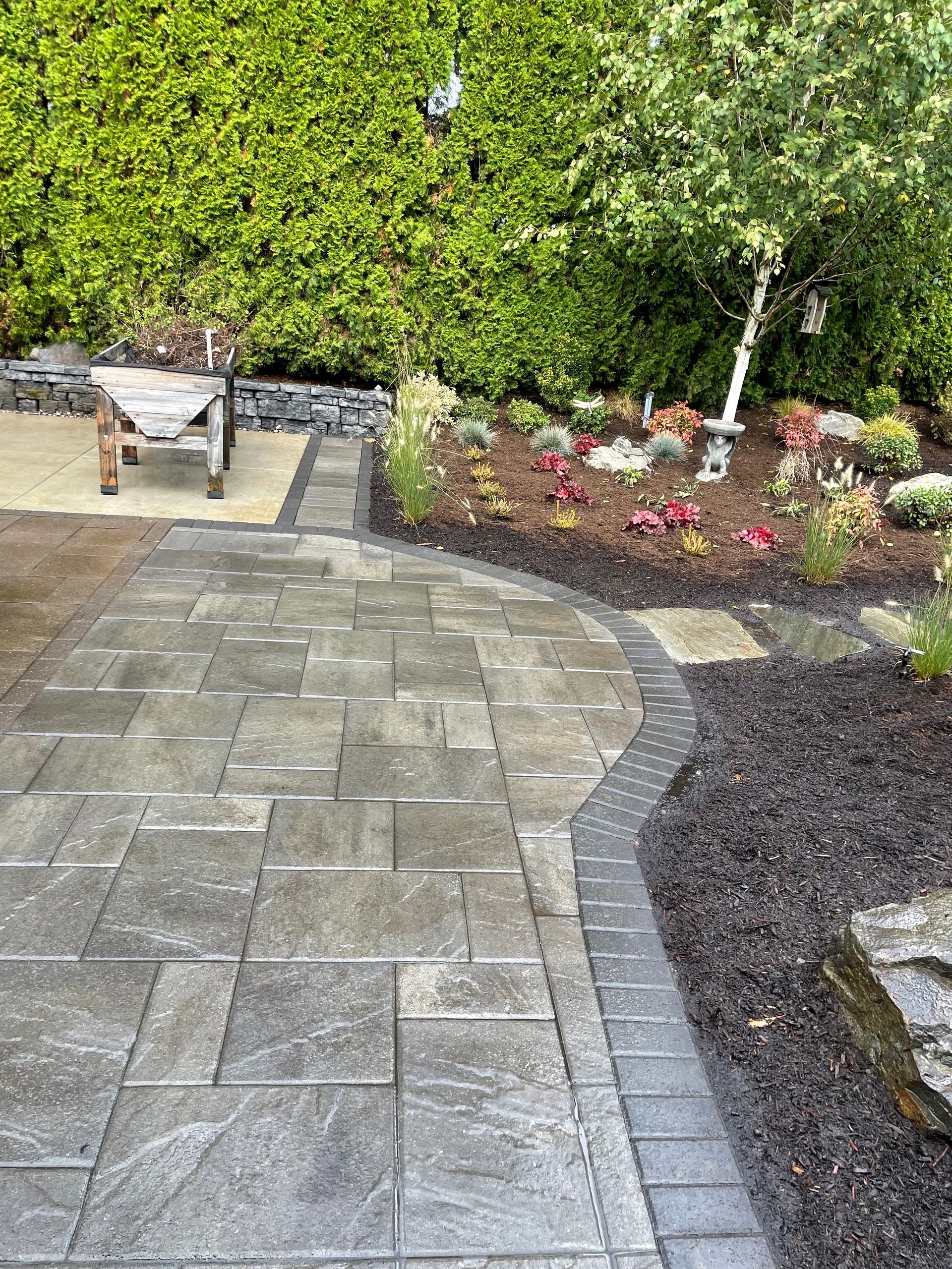 Stone patio path beside a flower bed and hedge in a landscaped garden