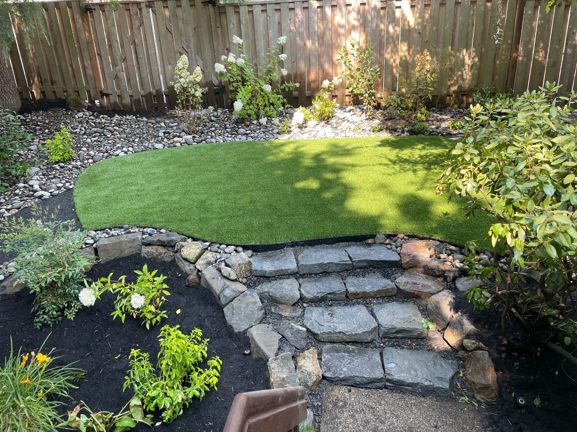 Backyard with stone steps leading to a raised grass lawn and fenced border garden