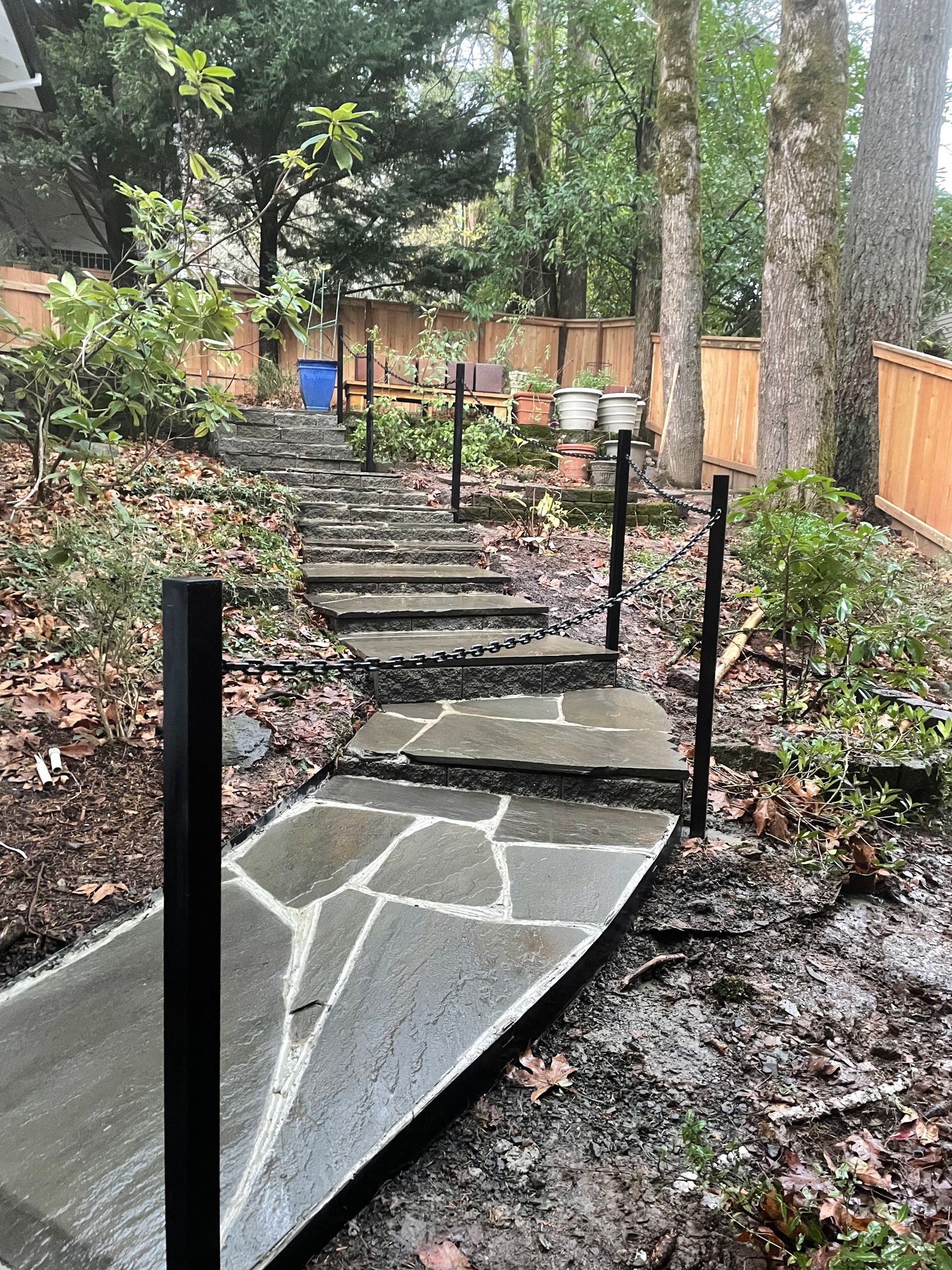 Steep stone steps with black railings ascending through a leafy outdoor garden path