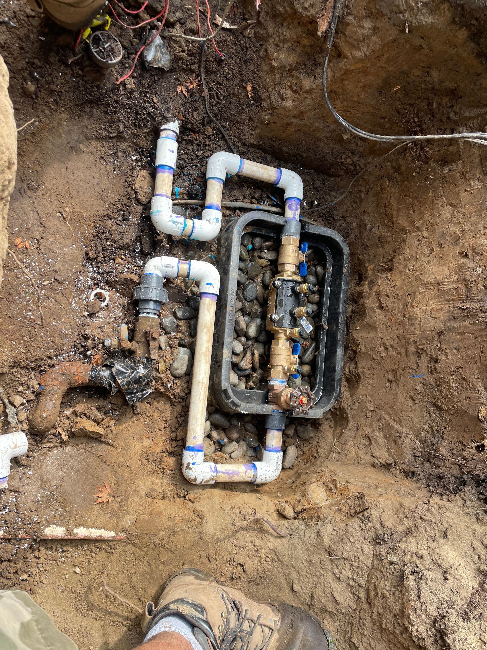 Exposed PVC plumbing pipes and fittings in a dirt trench during underground repair work