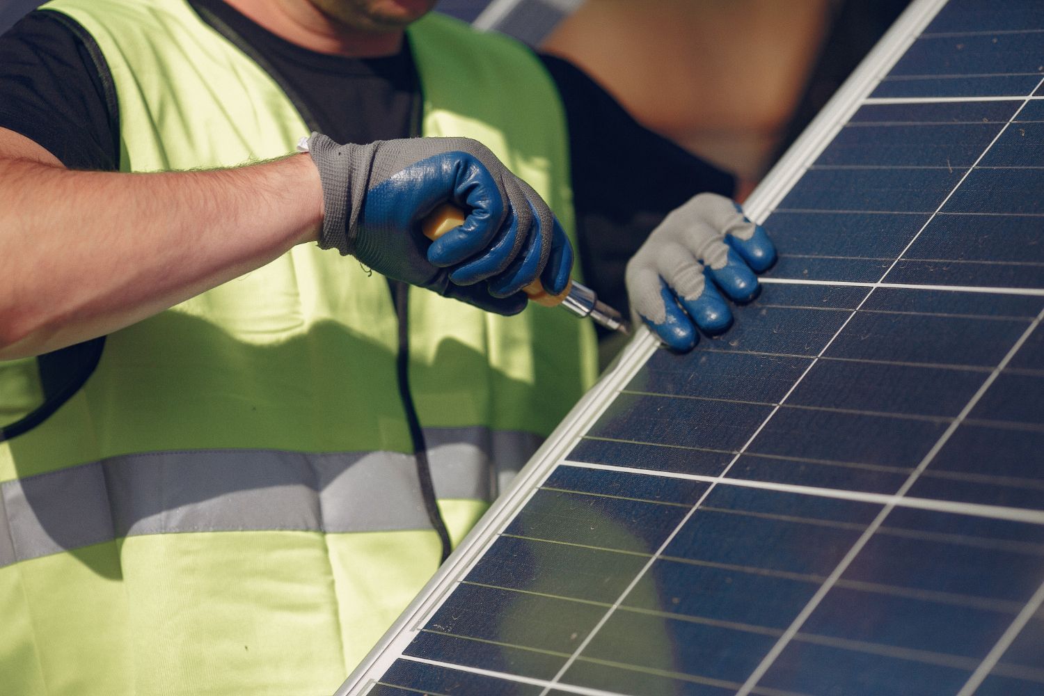 Worker in a safety vest installing a solar panel with a screwdriver