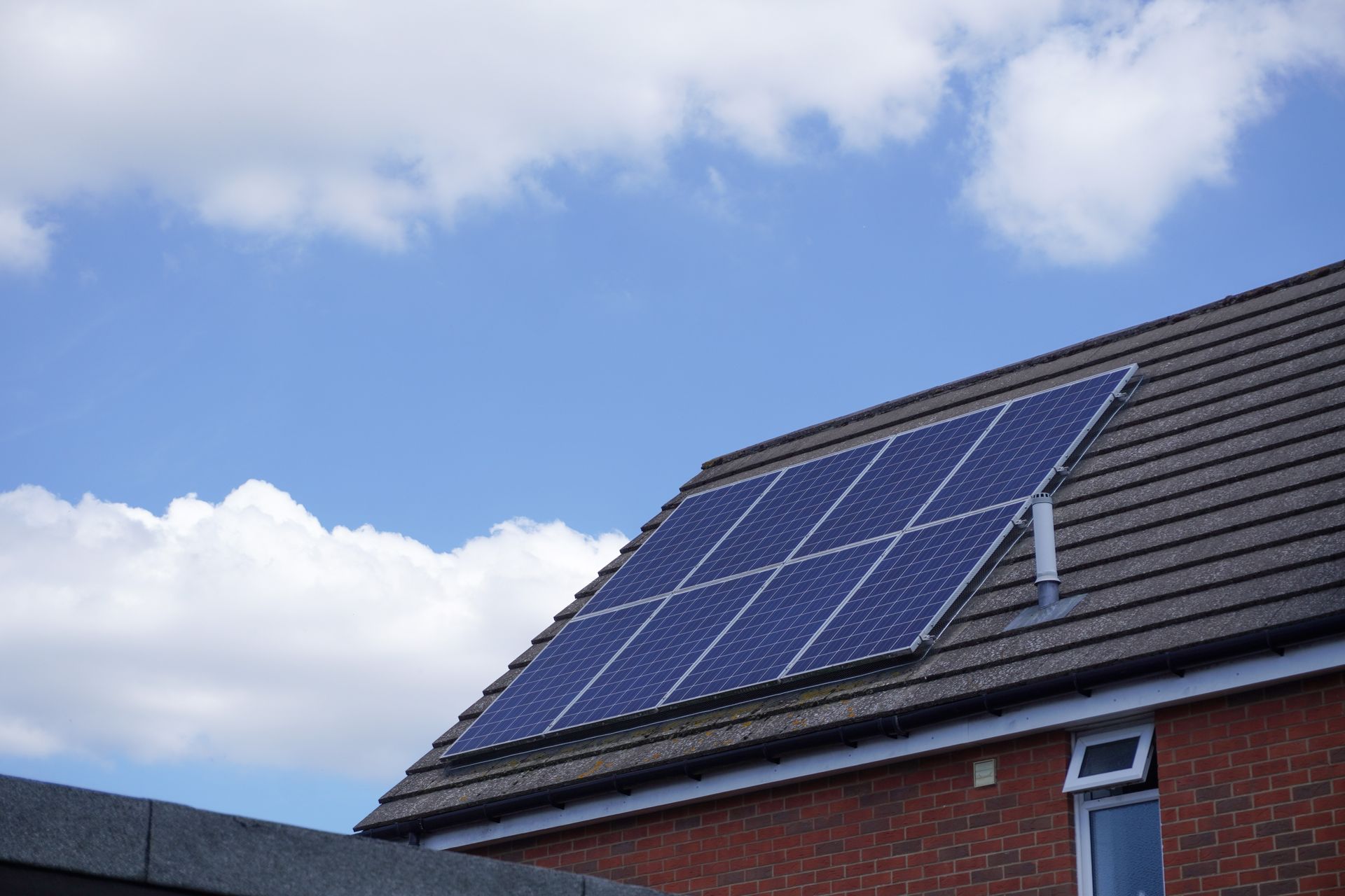 Solar panels on a residential roof, blue sky, white clouds, brick building.