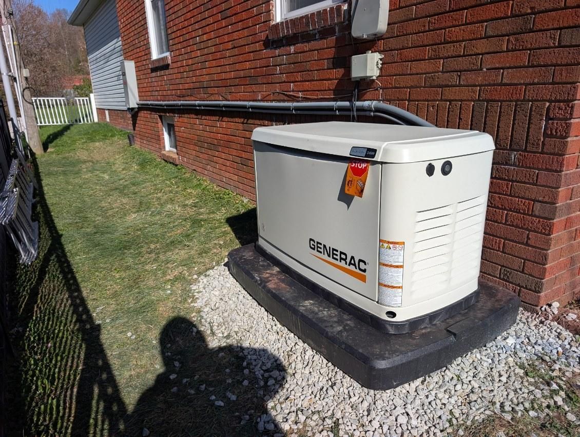 Outdoor generator unit beside a brick house, mounted on a concrete pad with gravel and grass nearby